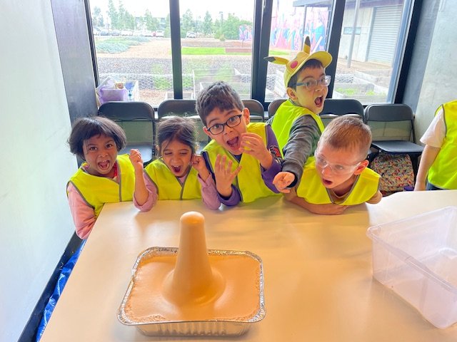 Children watching a foaming volcano experiment at Care Origin’s April 2026 holiday program