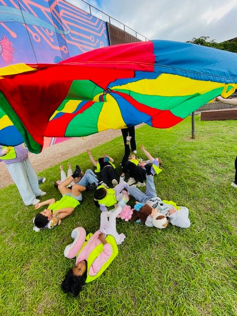 Children playing outdoors beneath a colourful parachute